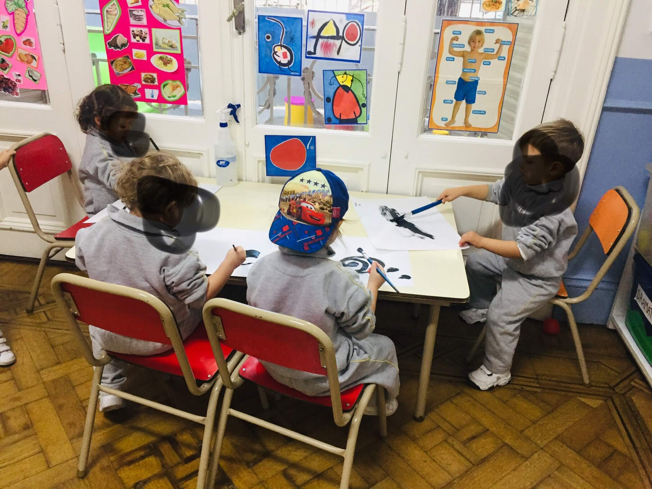 Trabajo en pequeños grupos en la sala Niños sentados en dos mesas del aula realizan distintas propuestas con materiales y hojas de trabajo.