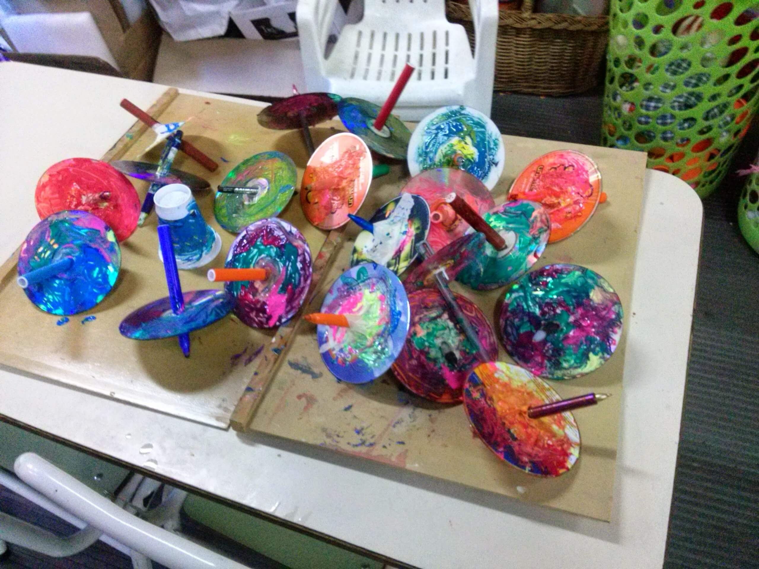 Trompos de colores construidos con discos reutilizados y lápices sobre una mesa de aula.