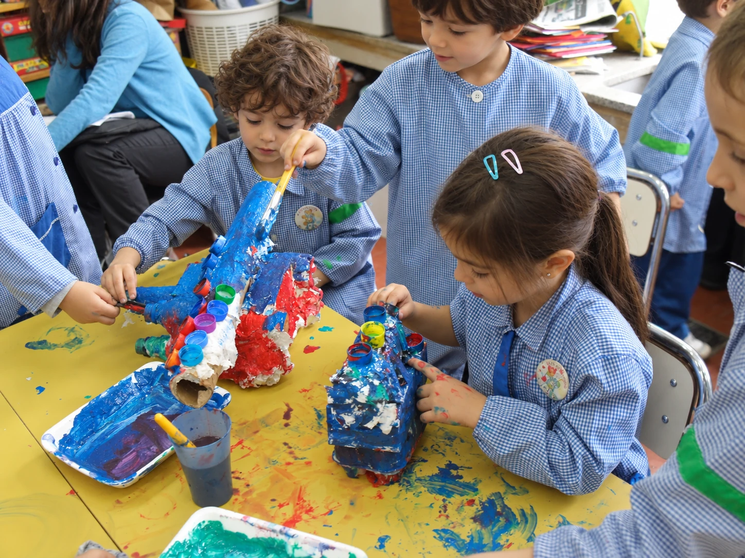 Exploración de pintura en pequeños grupos Recreación fotográfica de niños y niñas pintando construcciones de cartón con pinceles y témperas en pequeños grupos.
