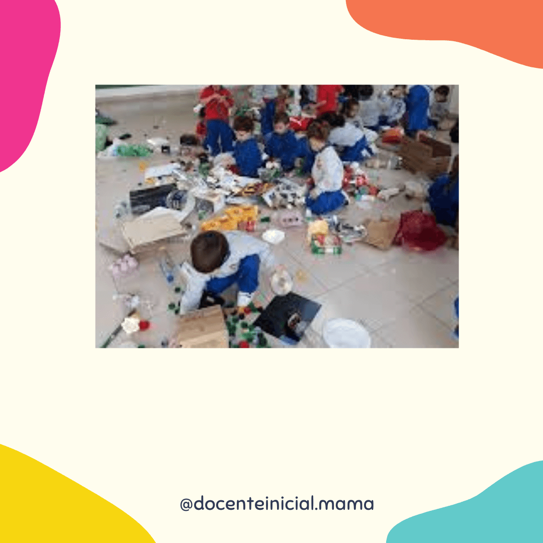Fotografía de varios niños en un aula o salón, sentados y agachados entre cajas, envases y otros objetos reutilizados esparcidos en el piso mientras exploran materiales de juego.