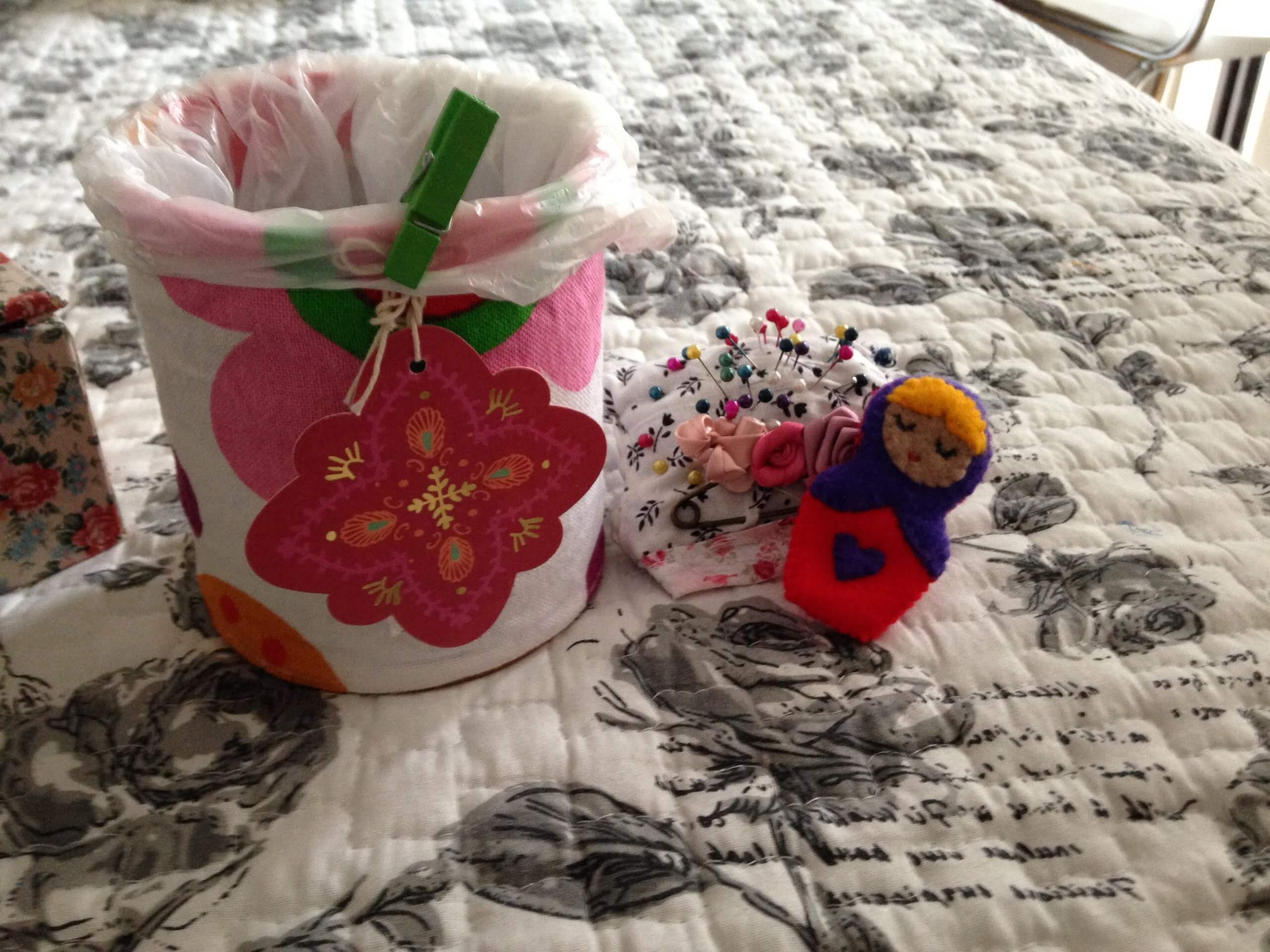 Títere de dedo de tela junto a un recipiente decorado con flores y materiales de costura.